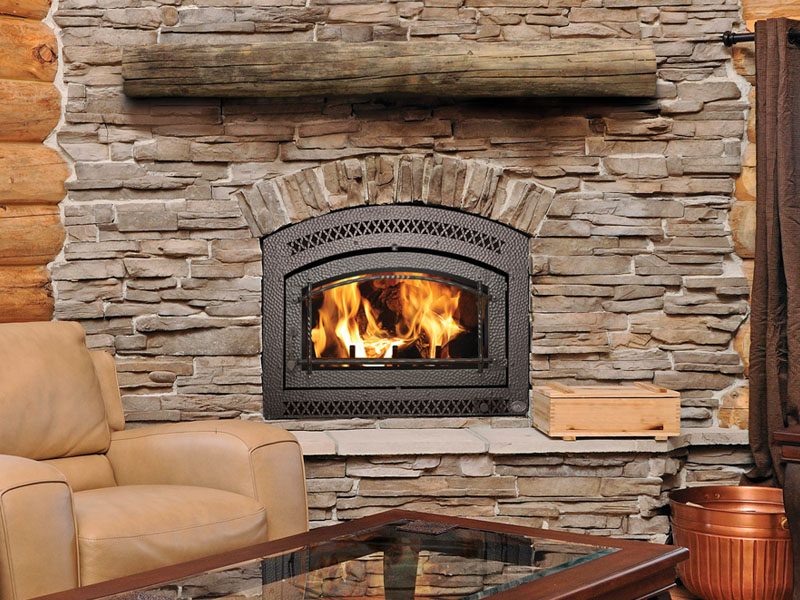 A lit fireplace in a stone wall, beside a comfy chair