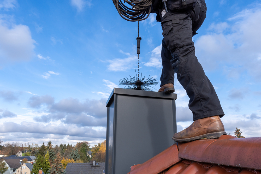 A man on the top of a roof, performing chimney sweeps, maintaining the chimney's cleanliness and functionality